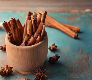 Paus de canela em um recipiente de madeira e estrelas de anis espalhadas sobre uma superfície, ilustrando os benefícios da canela para a saúde.