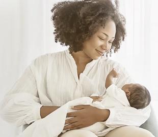 Mãe com cabelo cacheado segurando e olhando para seu bebê recém-nascido, simbolizando os benefícios do aleitamento materno para mães e bebês.