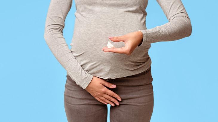 Mulher grávida segurando comprimidos na mão e tocando a região pélvica, simbolizando a preocupação com infecções vaginais e a saúde na gravidez.