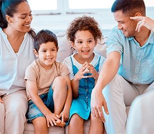 Família feliz com dois pais e duas crianças pequenas sentados juntos, simbolizando os cuidados médicos e benefícios do plano de saúde para todas as idades.
