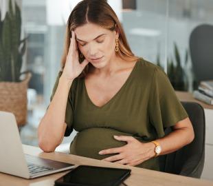 Mulher grávida com expressão preocupada segura a barriga e a cabeça, representando os impactos emocionais da gestação, como ansiedade e variações de humor.